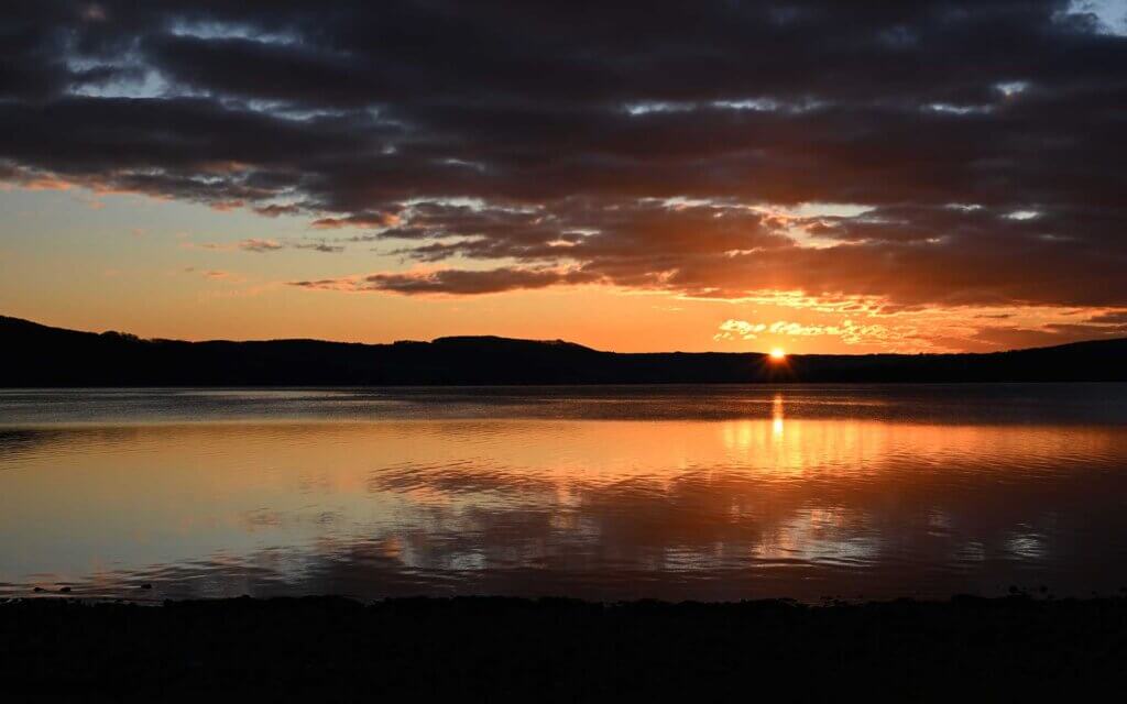 Bodenseeufer bei Abend mit Sonnenuntergang. In einer postfosillien Wirtschaft entstehen kaum mehr Treibhausgase. Unternehmen aus den Bereichen Wasser, Energie, Landwirtschaft, Kreislaufwirtschaft und Digitalisierung und könnten von der Dekarbonisierung profitieren.